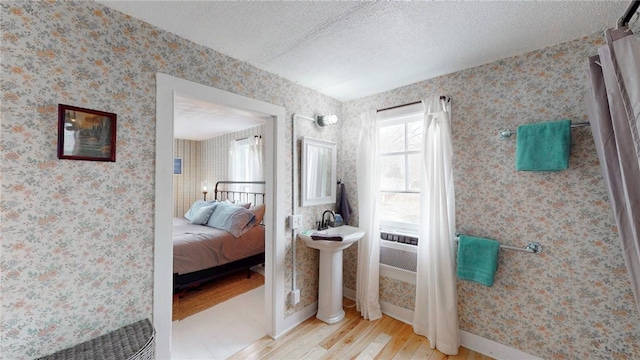 bedroom featuring baseboards, a textured ceiling, wood finished floors, and wallpapered walls