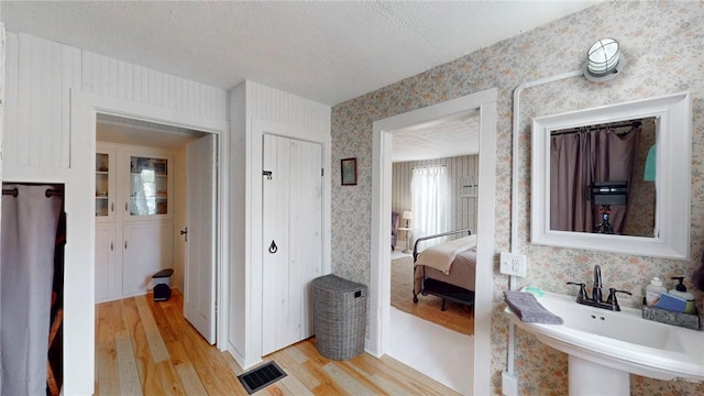 bathroom featuring wood finished floors, visible vents, wallpapered walls, a sink, and a textured ceiling