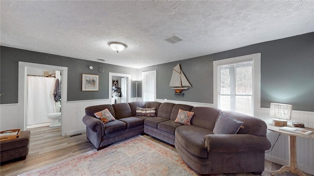 living room with a wainscoted wall, a textured ceiling, visible vents, and wood finished floors