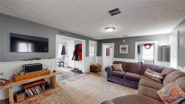 living area with visible vents, a textured ceiling, wood finished floors, and a wainscoted wall