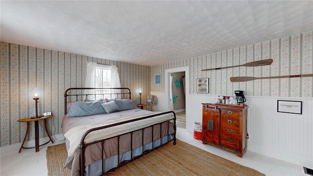 bedroom featuring wallpapered walls, visible vents, a wainscoted wall, and a textured ceiling