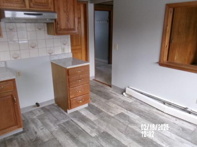 153 Holden Rd, Southport, NY 14871 - kitchen with under cabinet range hood, light wood-type flooring, baseboard heating, brown cabinets, and decorative backsplash