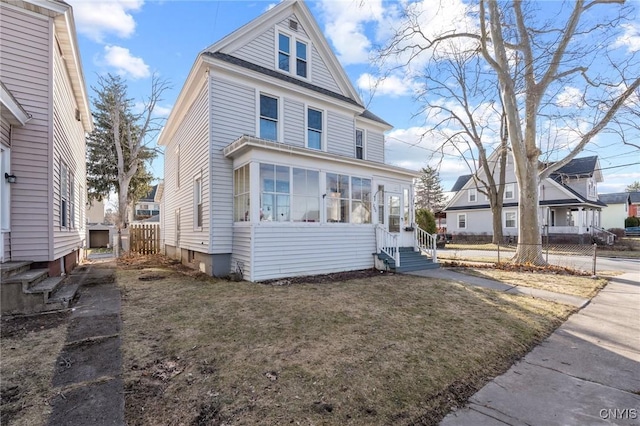 american foursquare style home featuring a sunroom, entry steps, a front yard, and fence