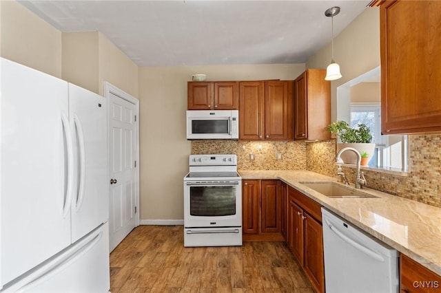 kitchen featuring brown cabinets, light wood-style flooring, a sink, white appliances, and light stone countertops