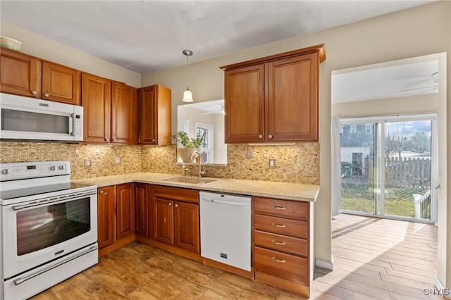 kitchen with a sink, white appliances, backsplash, and brown cabinetry