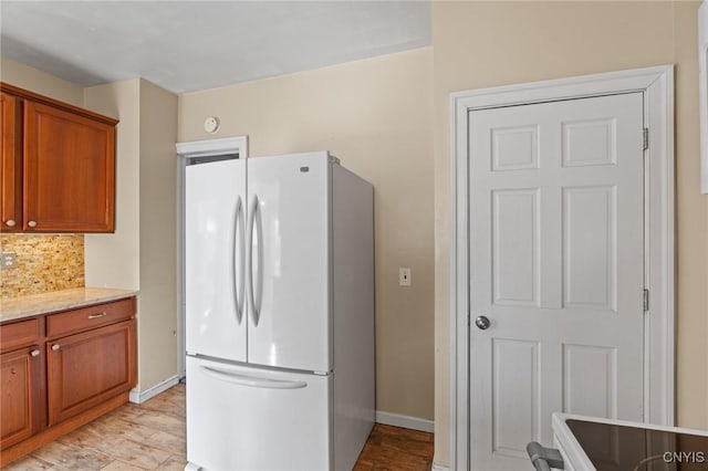 kitchen featuring brown cabinetry, backsplash, freestanding refrigerator, and baseboards