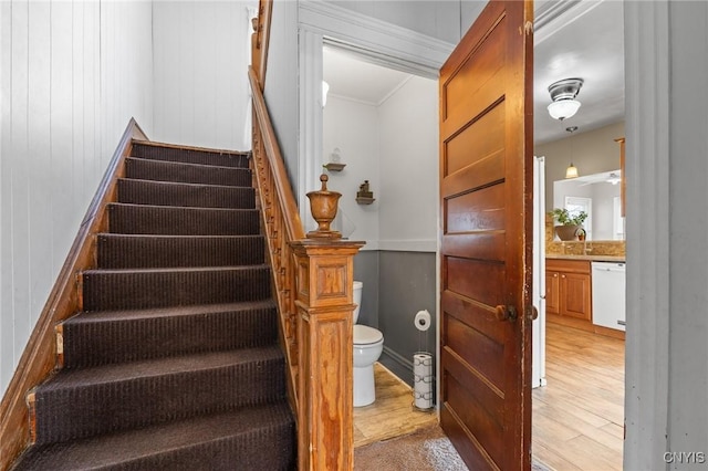 stairs featuring wood finished floors and crown molding