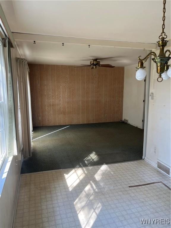 empty room featuring tile patterned floors, wooden walls, visible vents, and ceiling fan