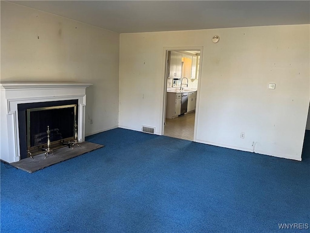 unfurnished living room with a fireplace with raised hearth, visible vents, carpet floors, and a sink