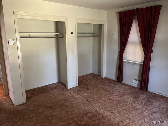 unfurnished bedroom featuring a baseboard heating unit, carpet, and two closets