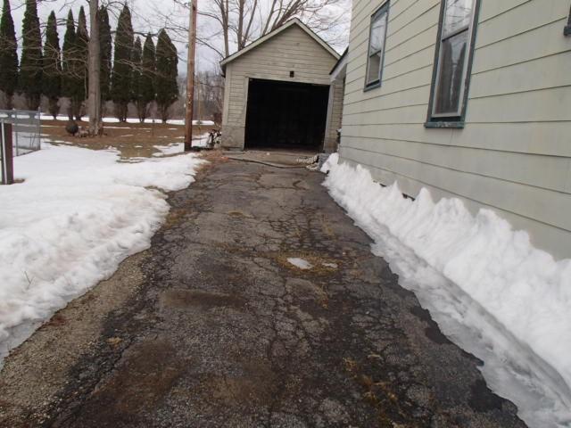 exterior space with aphalt driveway, a detached garage, and an outbuilding