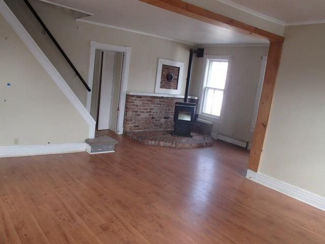 unfurnished living room featuring crown molding, stairs, baseboard heating, a wood stove, and wood finished floors