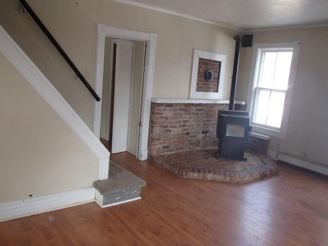 unfurnished living room with wood finished floors, baseboards, a wood stove, ornamental molding, and stairs