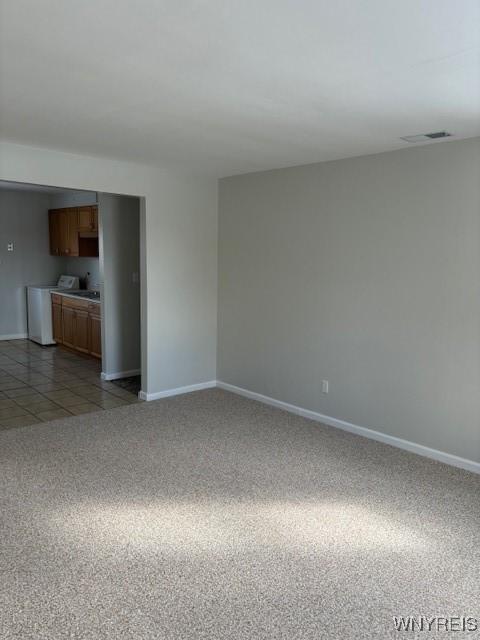 unfurnished living room featuring light tile patterned floors, visible vents, baseboards, washer / clothes dryer, and light colored carpet