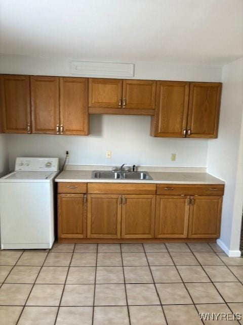 kitchen featuring light countertops, light tile patterned floors, brown cabinets, washer / clothes dryer, and a sink