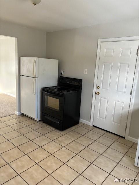 kitchen with light tile patterned floors, baseboards, black range with electric cooktop, and freestanding refrigerator