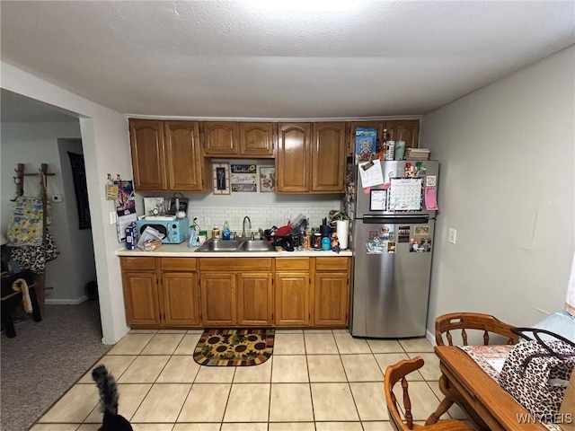 kitchen featuring a sink, brown cabinetry, light countertops, and freestanding refrigerator