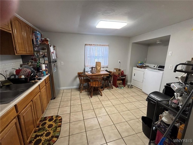 kitchen with independent washer and dryer, a sink, backsplash, brown cabinetry, and light tile patterned floors