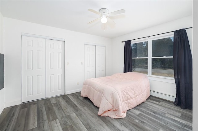 bedroom with wood finished floors, multiple closets, baseboard heating, and baseboards