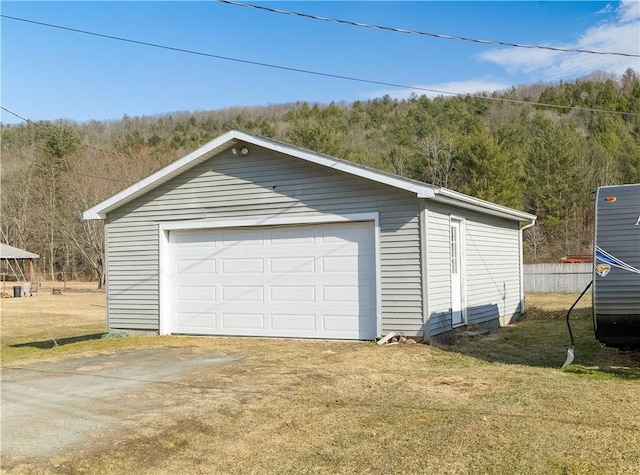 detached garage featuring fence and a view of trees