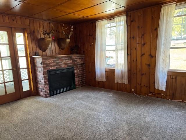 unfurnished living room with wooden walls, carpet, a fireplace, wood ceiling, and french doors