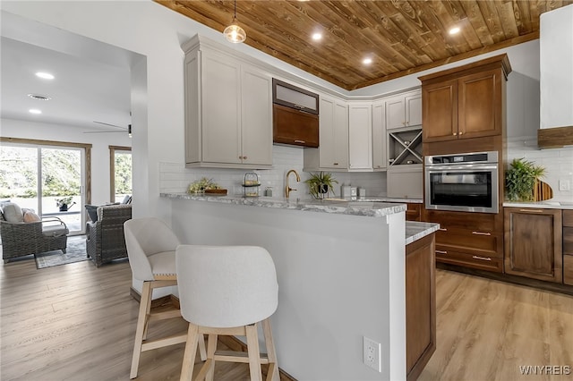 kitchen featuring backsplash, oven, light wood-style flooring, wooden ceiling, and a kitchen breakfast bar