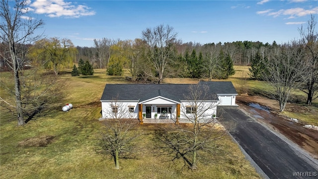 view of front facade featuring aphalt driveway, covered porch, a wooded view, and a front lawn