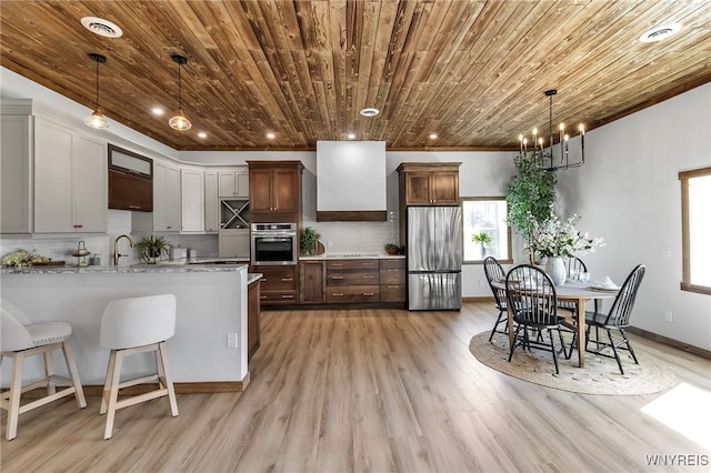 kitchen featuring tasteful backsplash, appliances with stainless steel finishes, a peninsula, wall chimney range hood, and wood ceiling