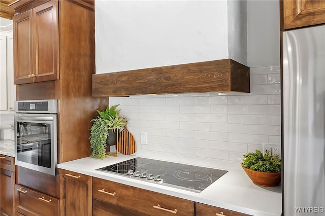 kitchen featuring oven, black electric stovetop, decorative backsplash, custom exhaust hood, and refrigerator