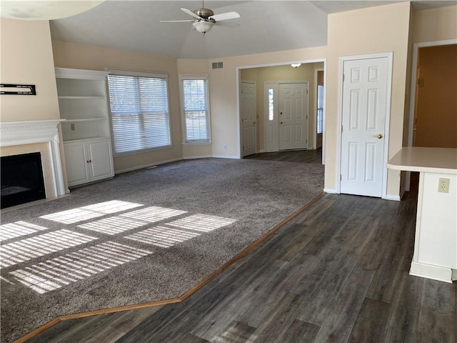 unfurnished living room featuring baseboards, visible vents, dark wood-style flooring, ceiling fan, and vaulted ceiling