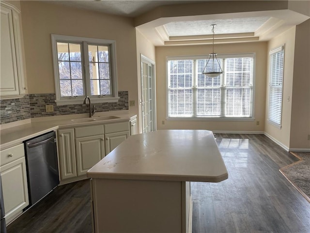 kitchen featuring a center island, light countertops, a tray ceiling, stainless steel dishwasher, and a sink