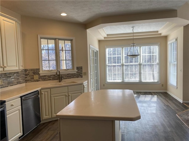 kitchen with a sink, a tray ceiling, tasteful backsplash, light countertops, and dishwashing machine