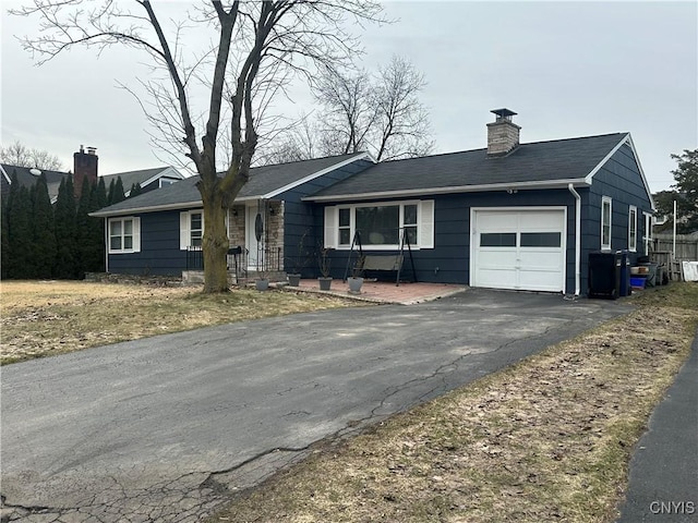 ranch-style home with an attached garage, a chimney, and driveway