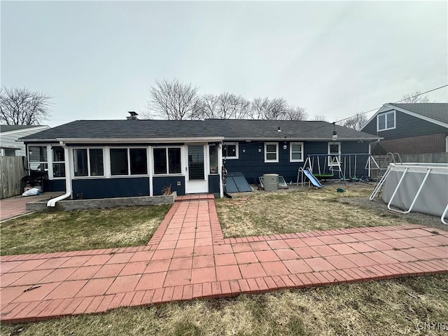 back of property with a shingled roof, an empty pool, a playground, and fence