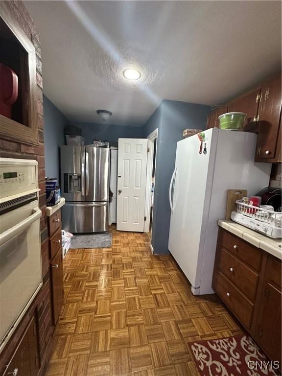 kitchen featuring white appliances, tile counters, and a textured ceiling