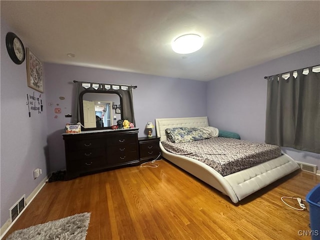 bedroom with wood finished floors, visible vents, and baseboards