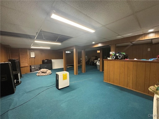 finished basement featuring a paneled ceiling, carpet floors, and wood walls