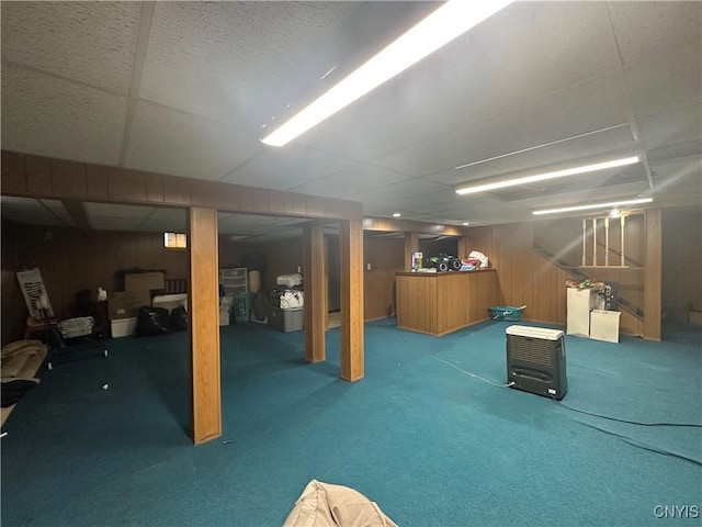 finished basement with wooden walls, a drop ceiling, and carpet floors