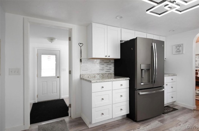 kitchen with stainless steel fridge with ice dispenser, decorative backsplash, light wood-style flooring, arched walkways, and white cabinetry