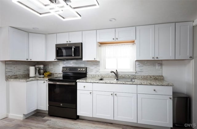 kitchen with light stone counters, a sink, white cabinets, black range with electric stovetop, and stainless steel microwave