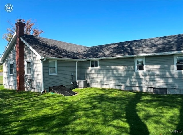 rear view of house with central AC unit, a lawn, a chimney, and roof with shingles