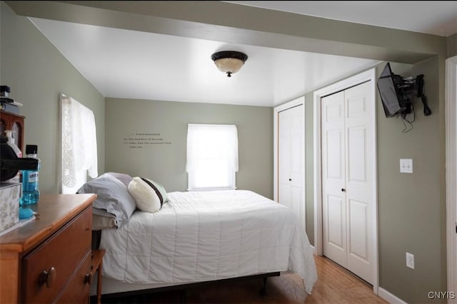 bedroom featuring light wood-style floors, baseboards, and two closets