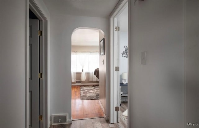 corridor featuring arched walkways, visible vents, and light wood-style floors