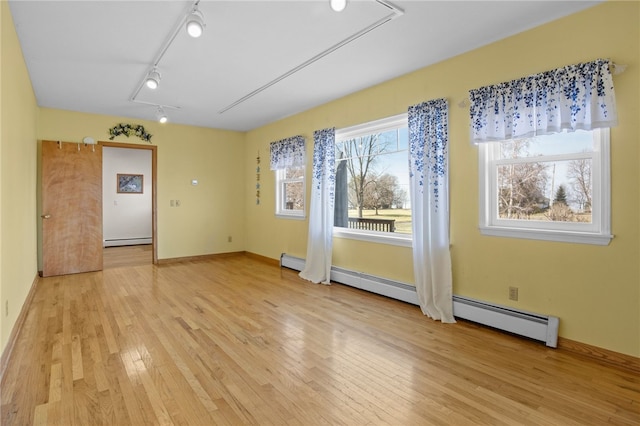 spare room featuring track lighting, a baseboard heating unit, light wood finished floors, baseboard heating, and attic access