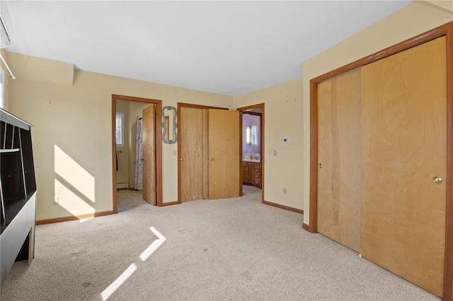 unfurnished bedroom featuring a baseboard radiator, multiple closets, light colored carpet, and ensuite bathroom