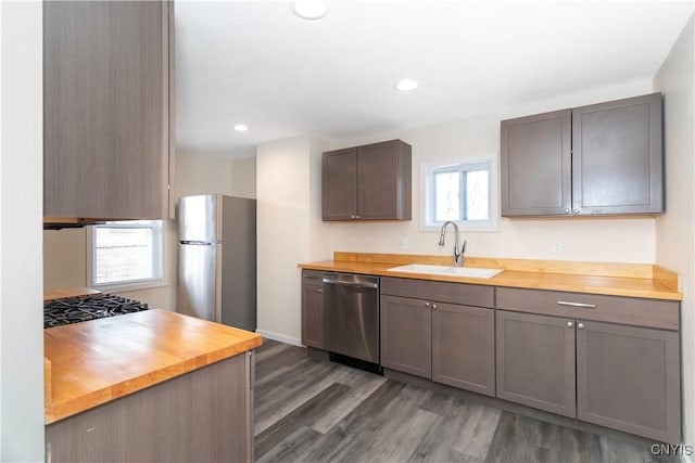 kitchen featuring wood finished floors, recessed lighting, a sink, stainless steel appliances, and wood counters