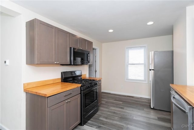 kitchen featuring baseboards, recessed lighting, dark wood-style flooring, butcher block countertops, and stainless steel appliances