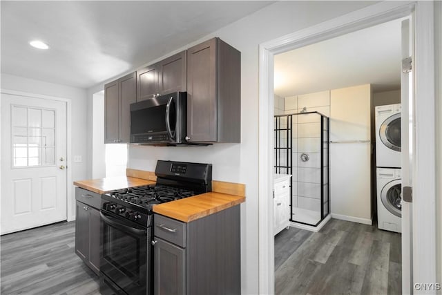 kitchen featuring dark wood-style flooring, black gas range, wood counters, stainless steel microwave, and stacked washer / dryer