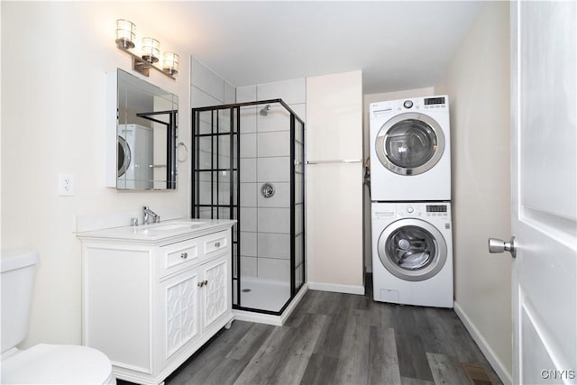 clothes washing area with a sink, dark wood-style floors, stacked washer / dryer, baseboards, and laundry area