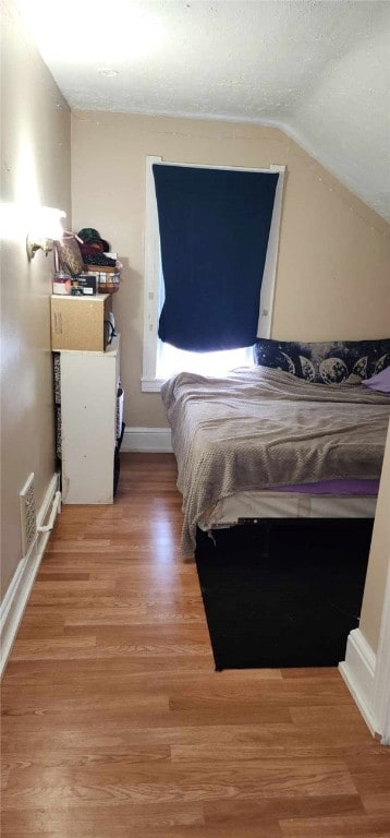 bedroom with light wood-type flooring, visible vents, a textured ceiling, baseboards, and vaulted ceiling